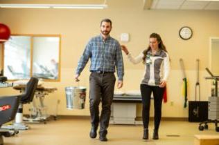 Therapist helps patient walk during therapy session.