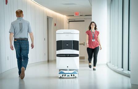 图中，TUG机器人在医院走廊上行走，机器人两侧各走两个人.